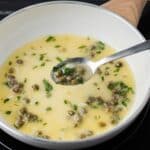 Lemon caper sauce in skillet with a spoon taking some out.