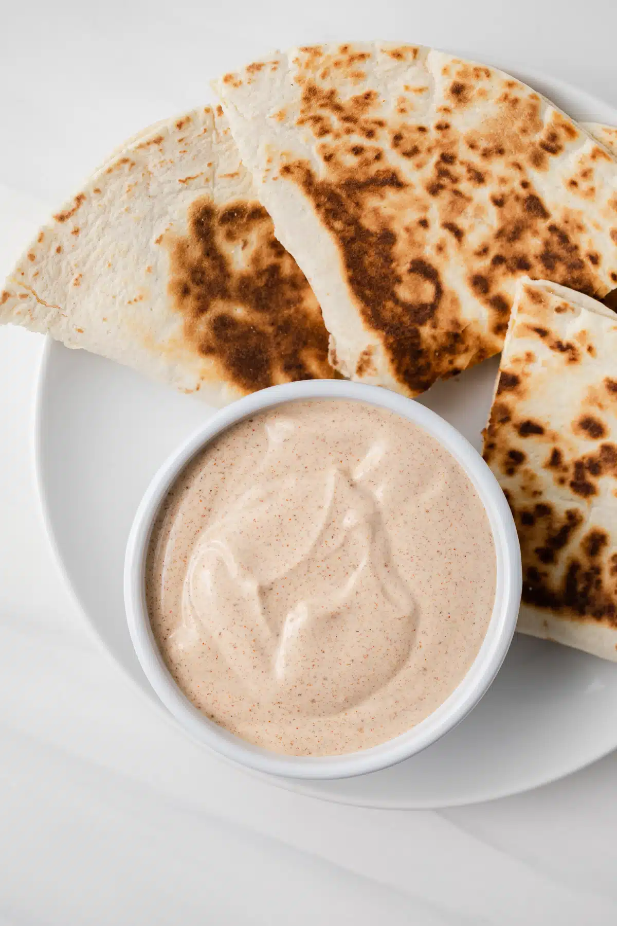 Overhead of quesadilla sauce in white bowl on plate with quesadillas.