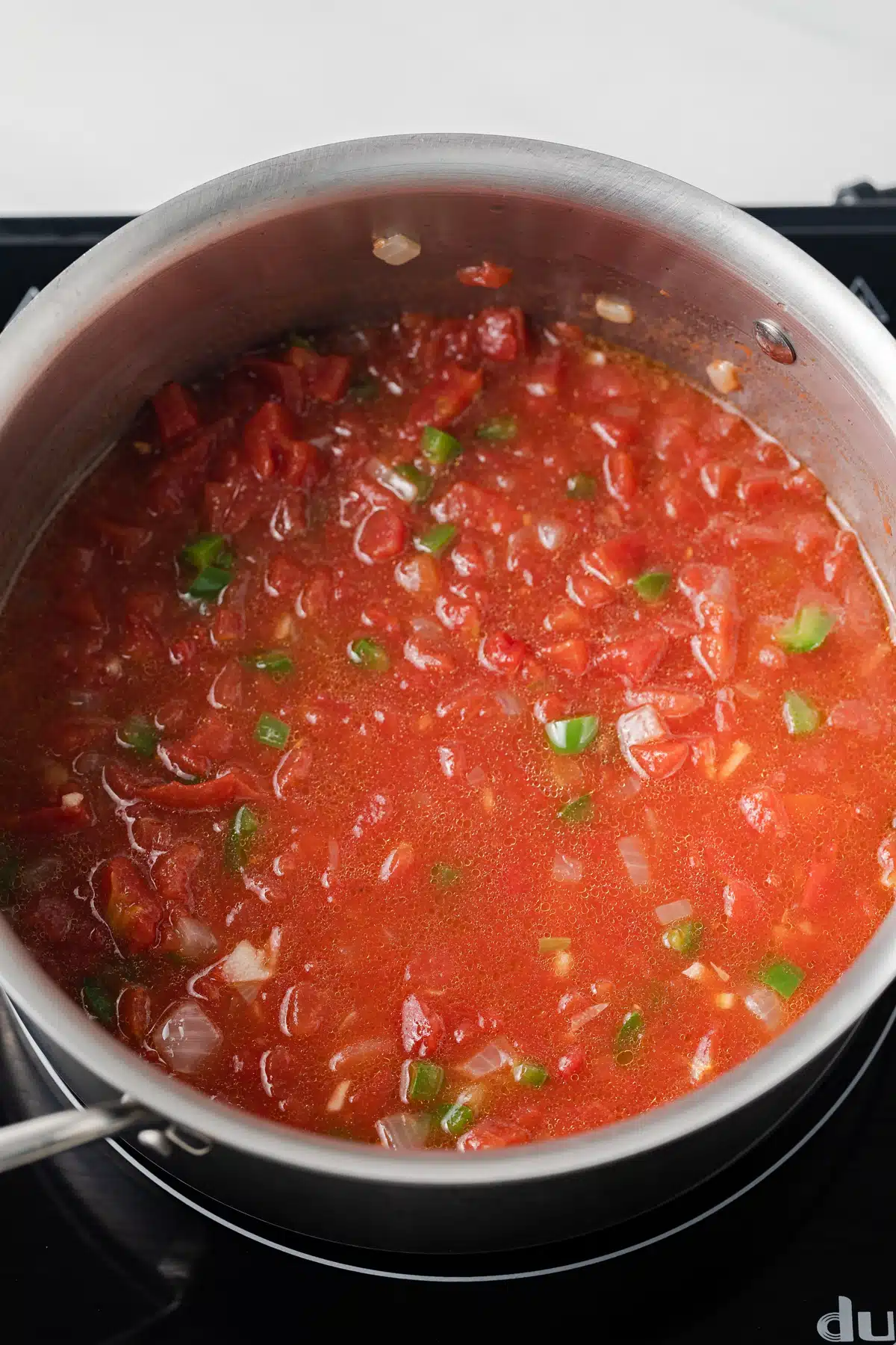 Tomatoes with peppers, onions, and garlic in saucepan.
