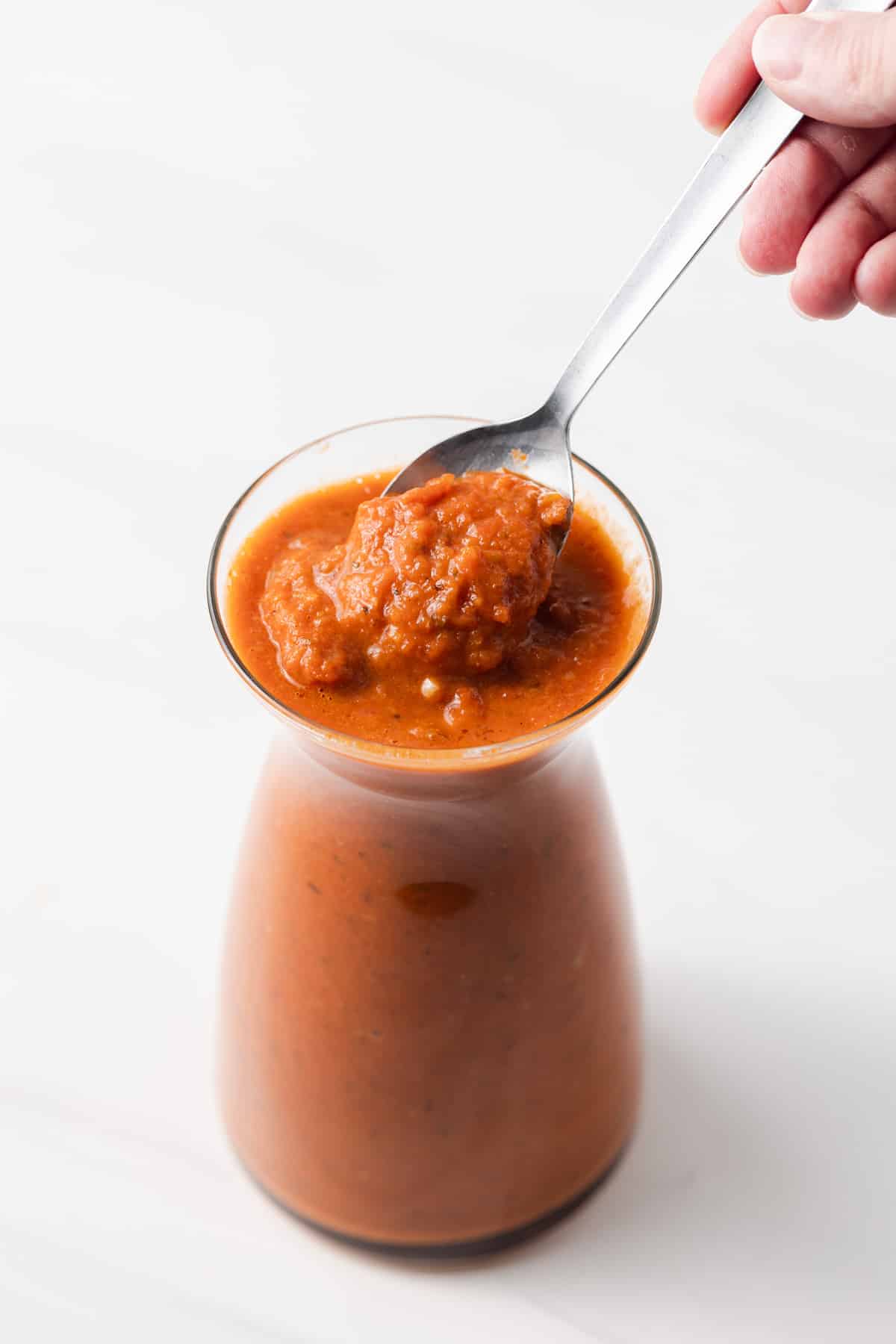 Spoon taking out ranchero sauce out of jar.