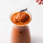 Spoon taking out ranchero sauce out of jar.