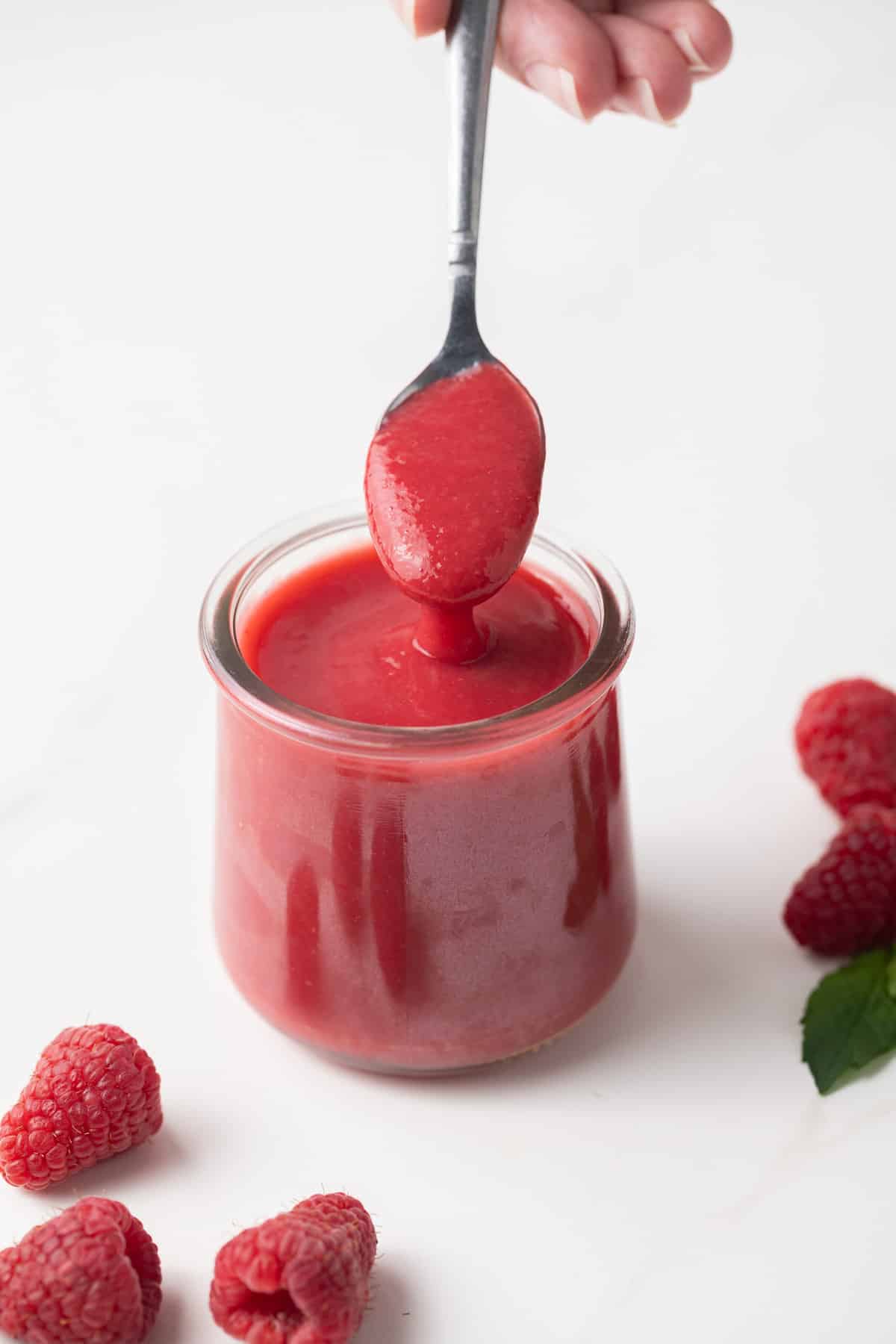 Raspberry sauce in a glass jar with a spoon.