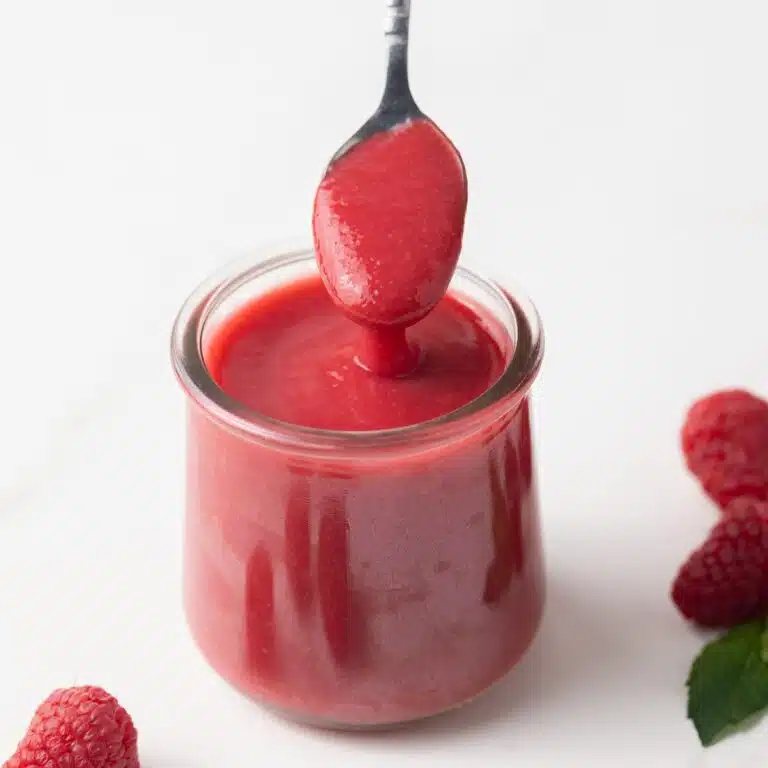 Raspberry sauce in a glass jar with a spoon.