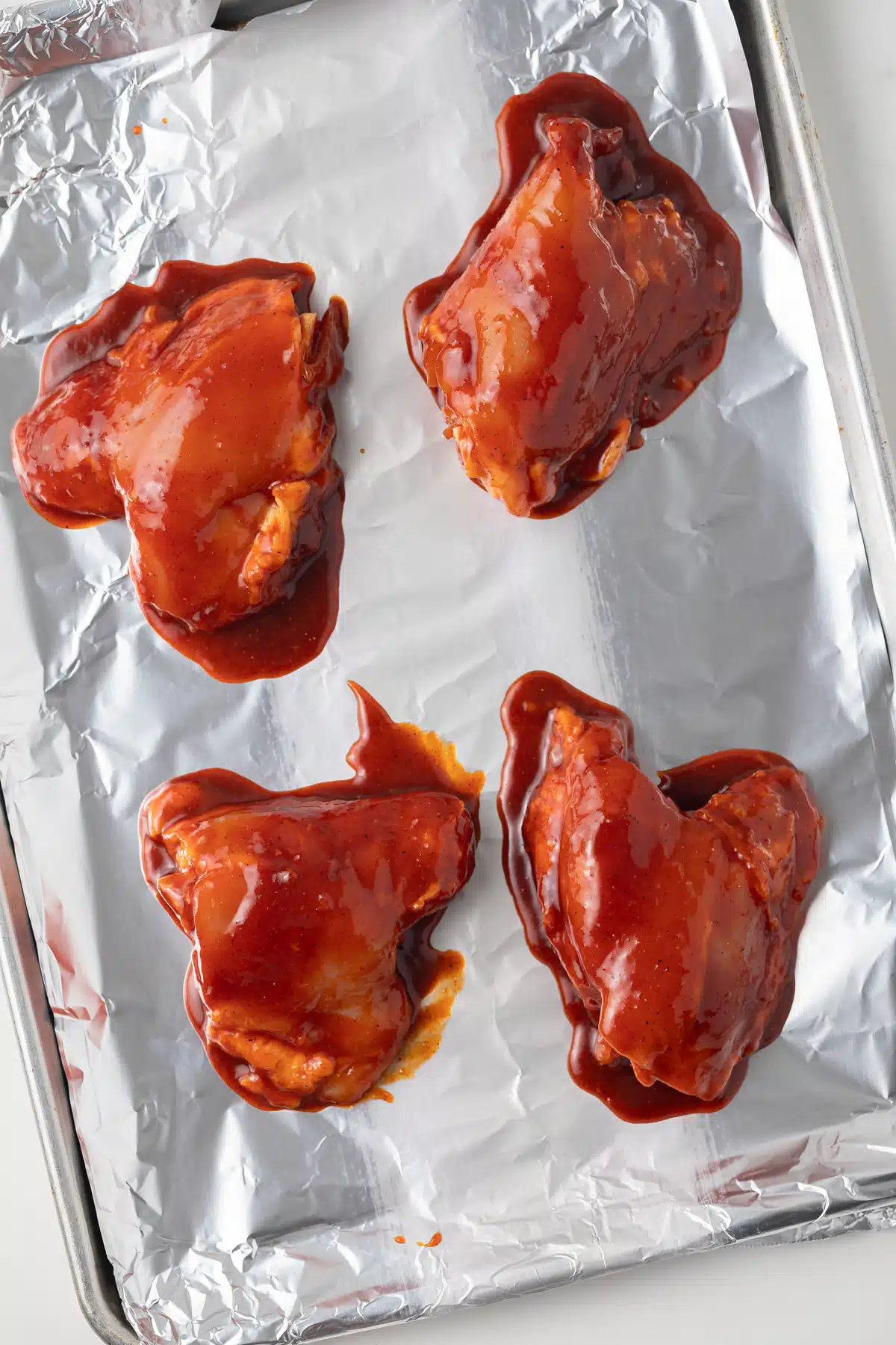 Chicken coated in spicy marinade on baking sheet.