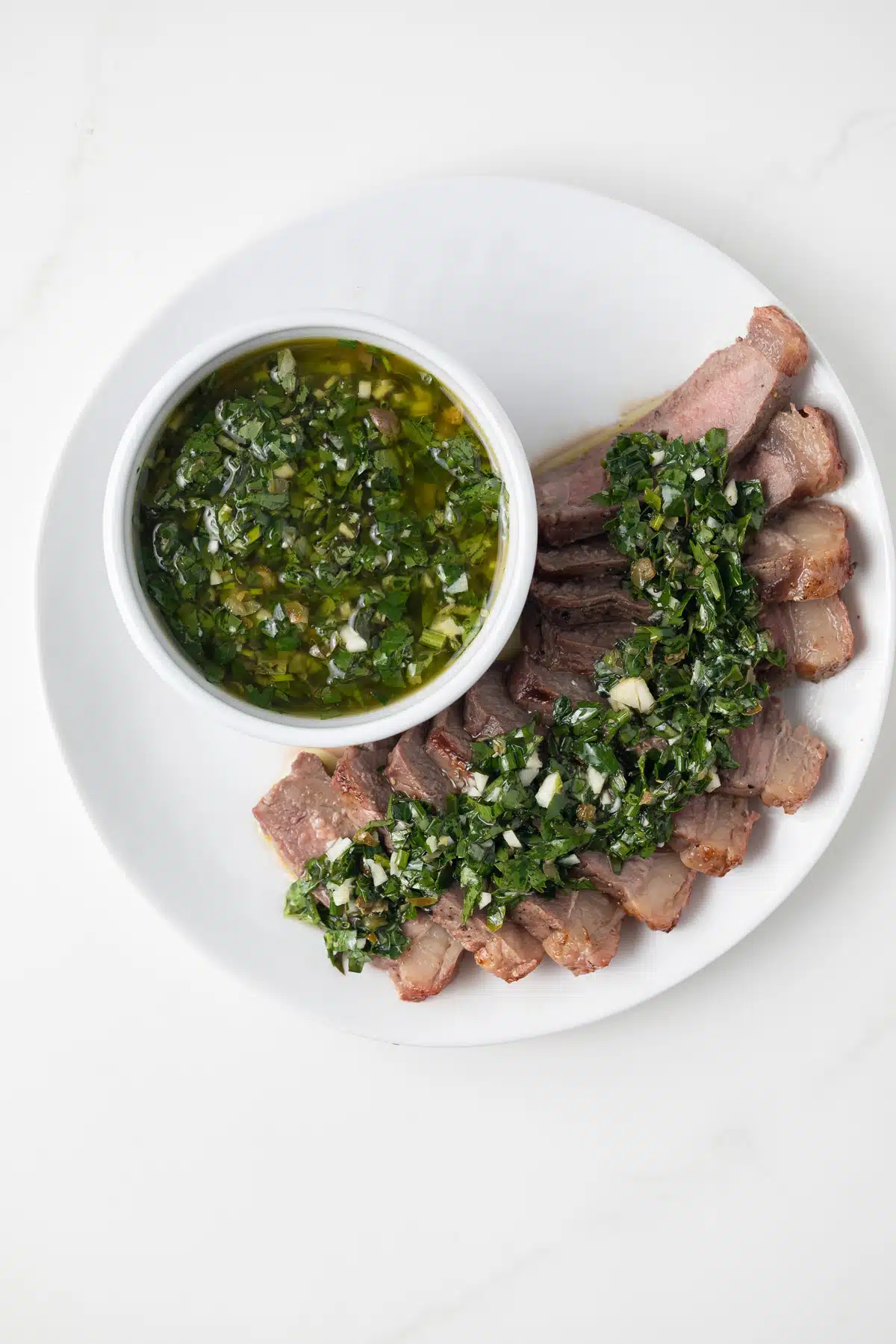 Herb caper sauce drizzled over steak slices.