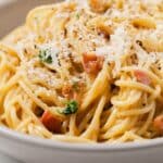Close up of carbonara sauce over spaghetti noodles.