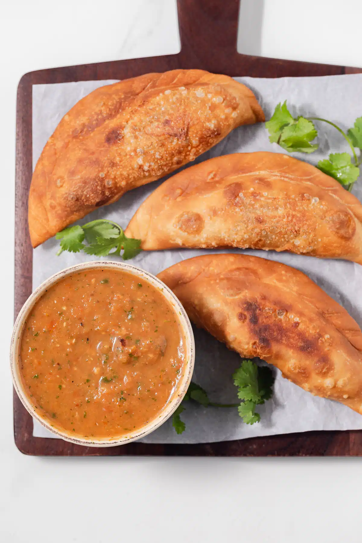 Overhead of empanada dipping sauce with three empanadas.