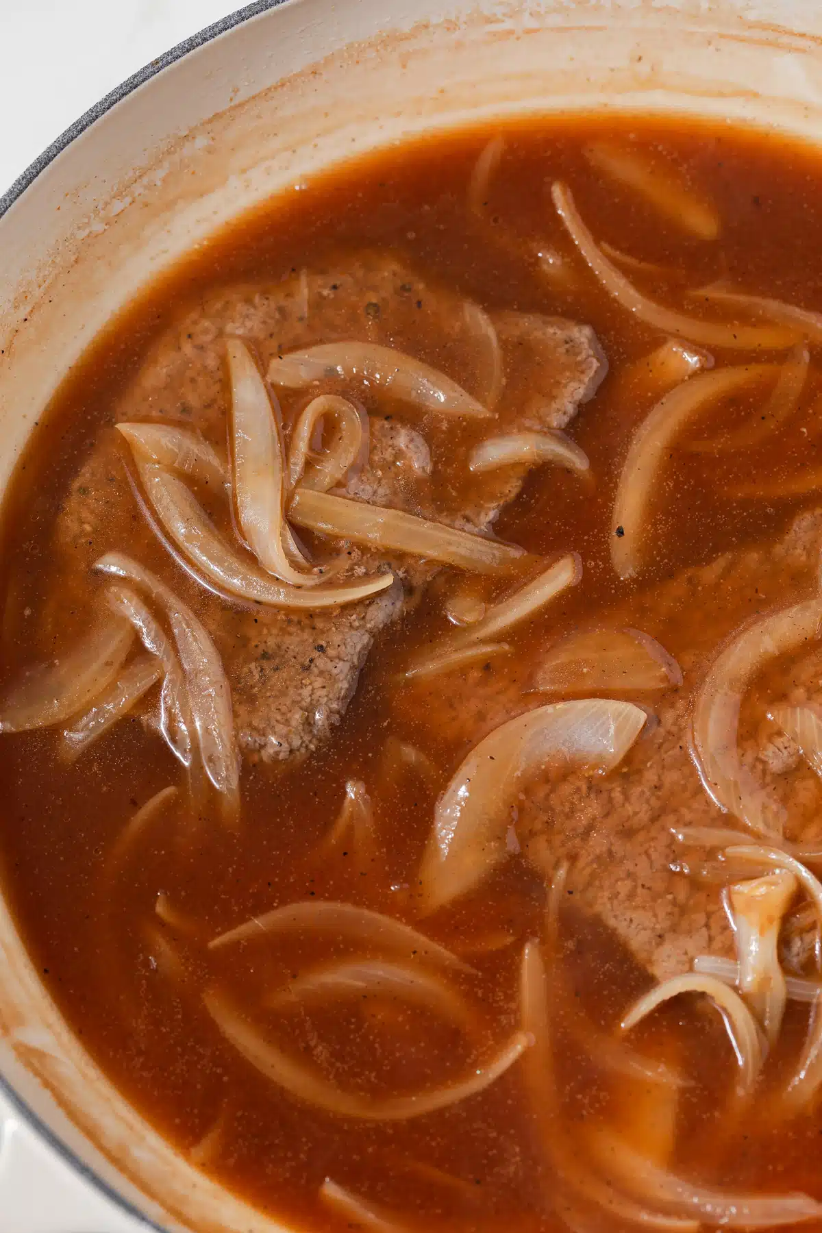 Close up of steaks and salisbury steak sauce in pan.