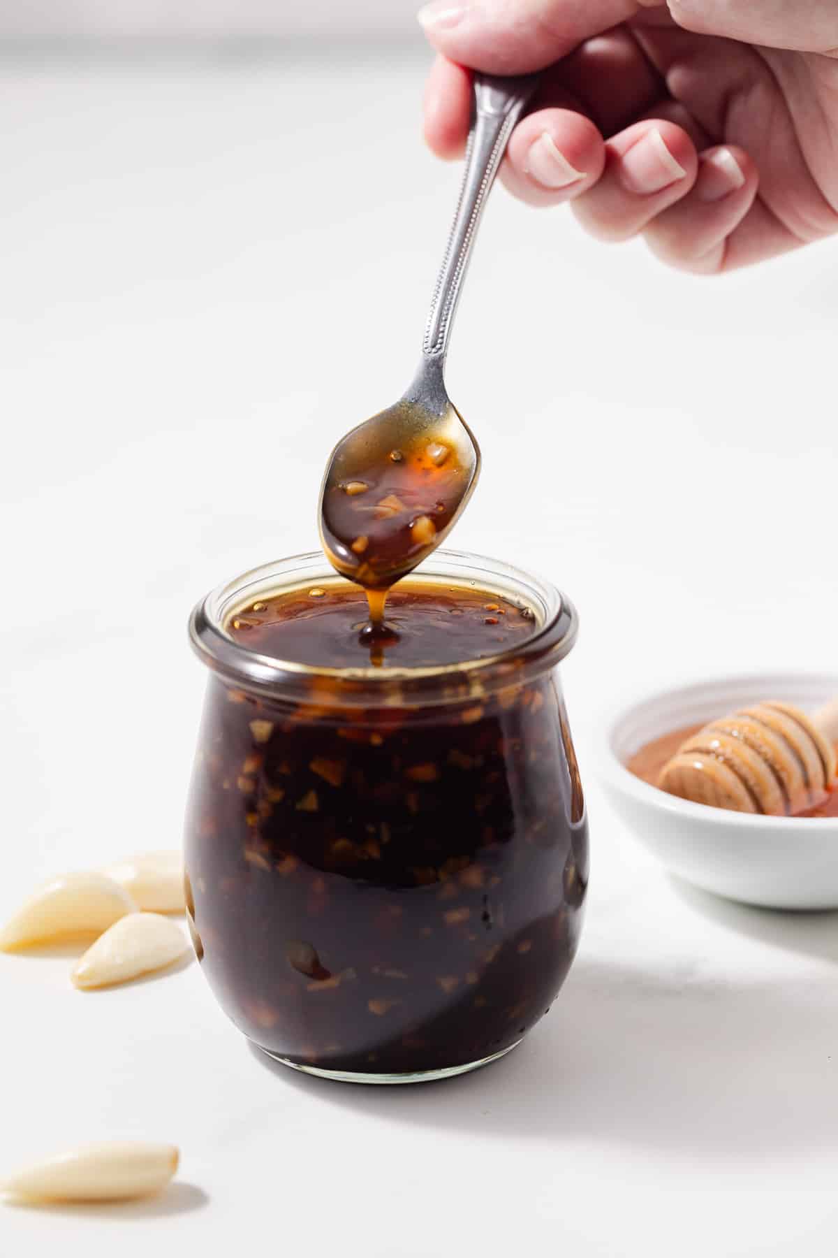 A spoon scooping out honey garlic sauce from a jar.