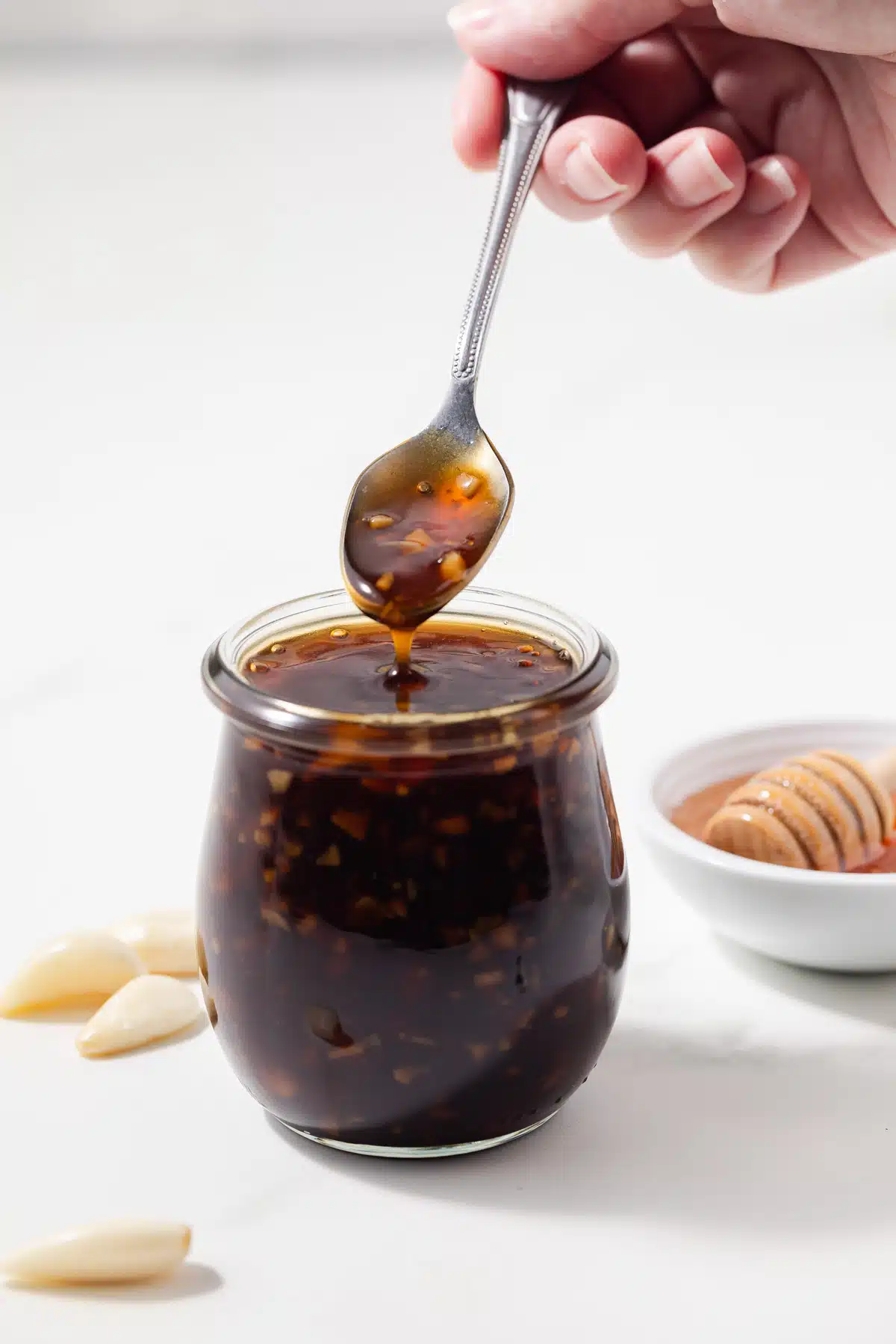 A spoon scooping out honey garlic sauce from a jar.