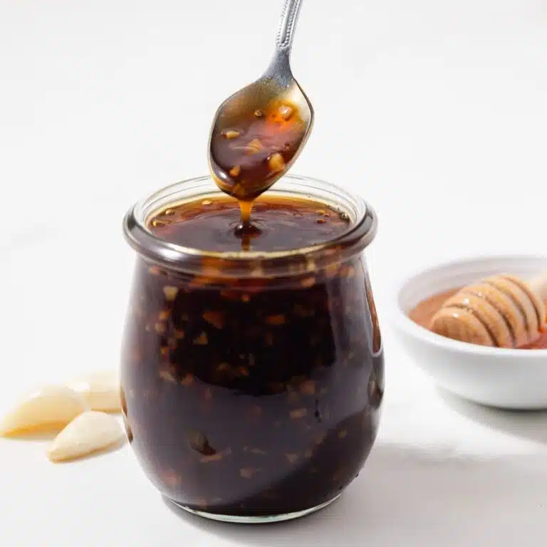 A spoon scooping out honey garlic sauce from a jar.