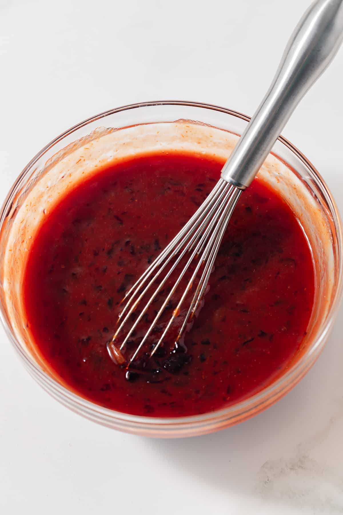 Meatball sauce in glass bowl with whisk.
