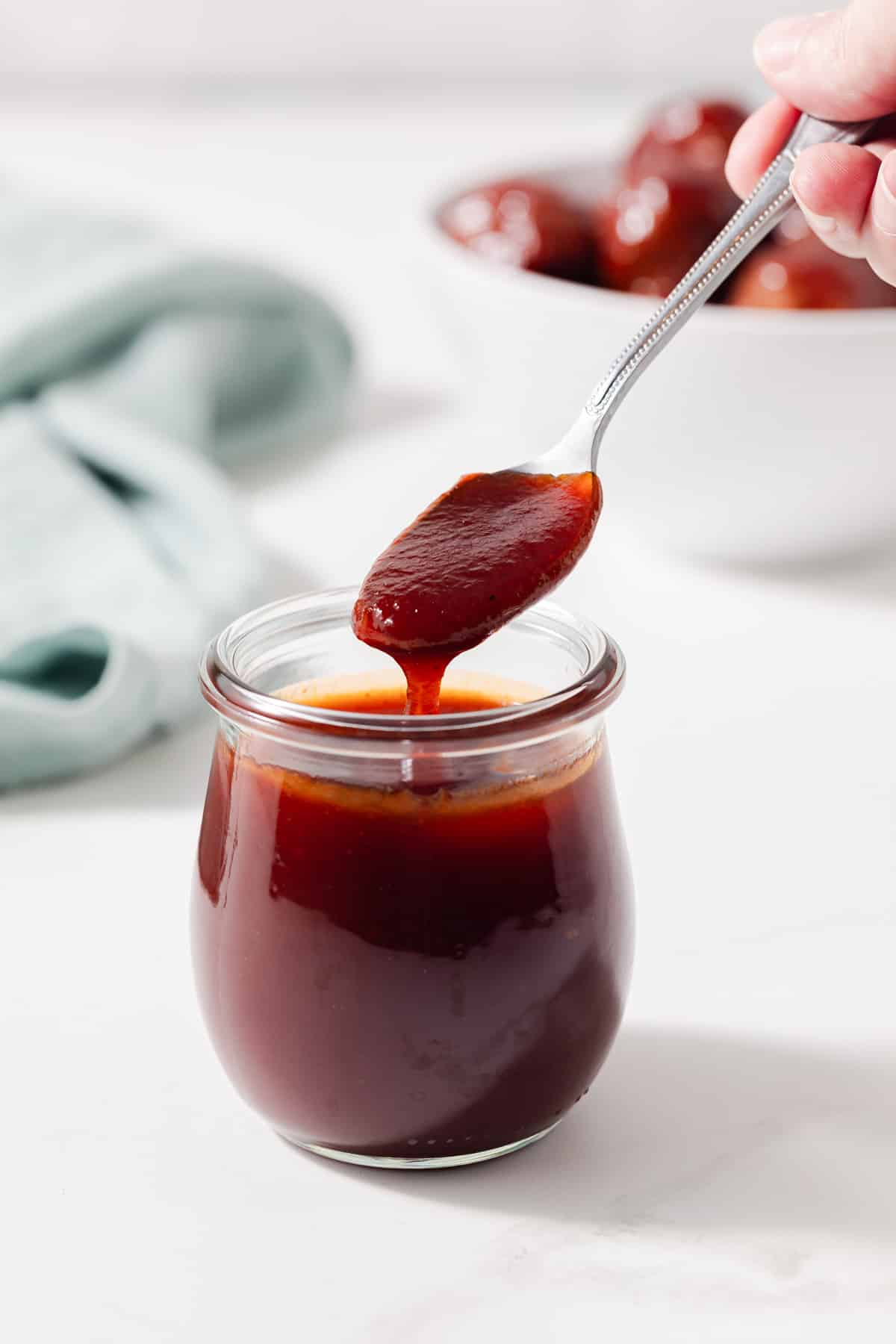 A spoon scooping meatball sauce out of a glass jar.