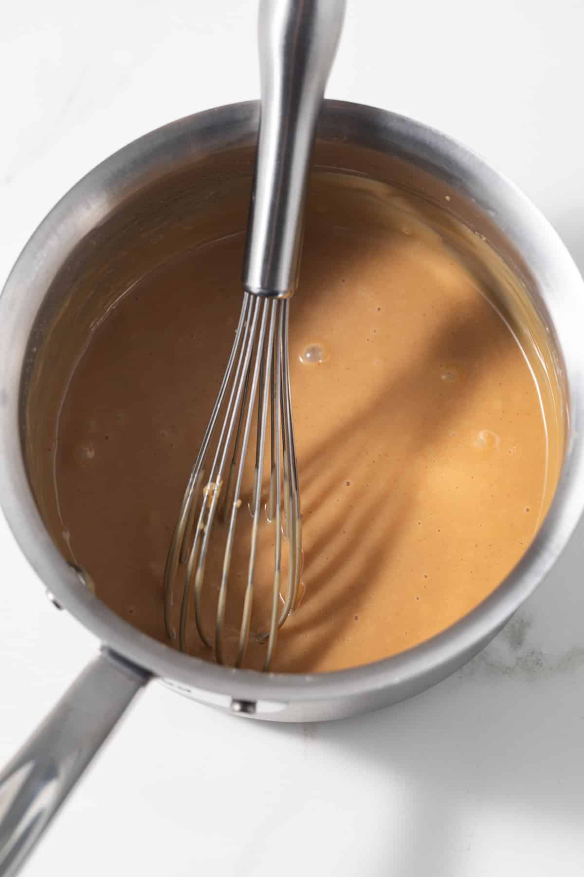 Peanut butter sauce in a saucepan with whisk.