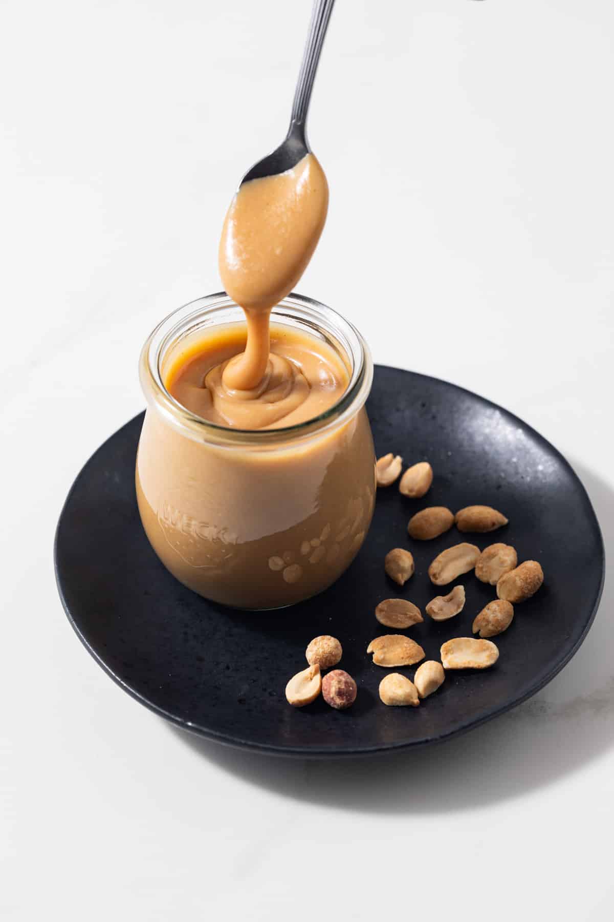 Creamy peanut butter sauce spooned out of a glass jar.