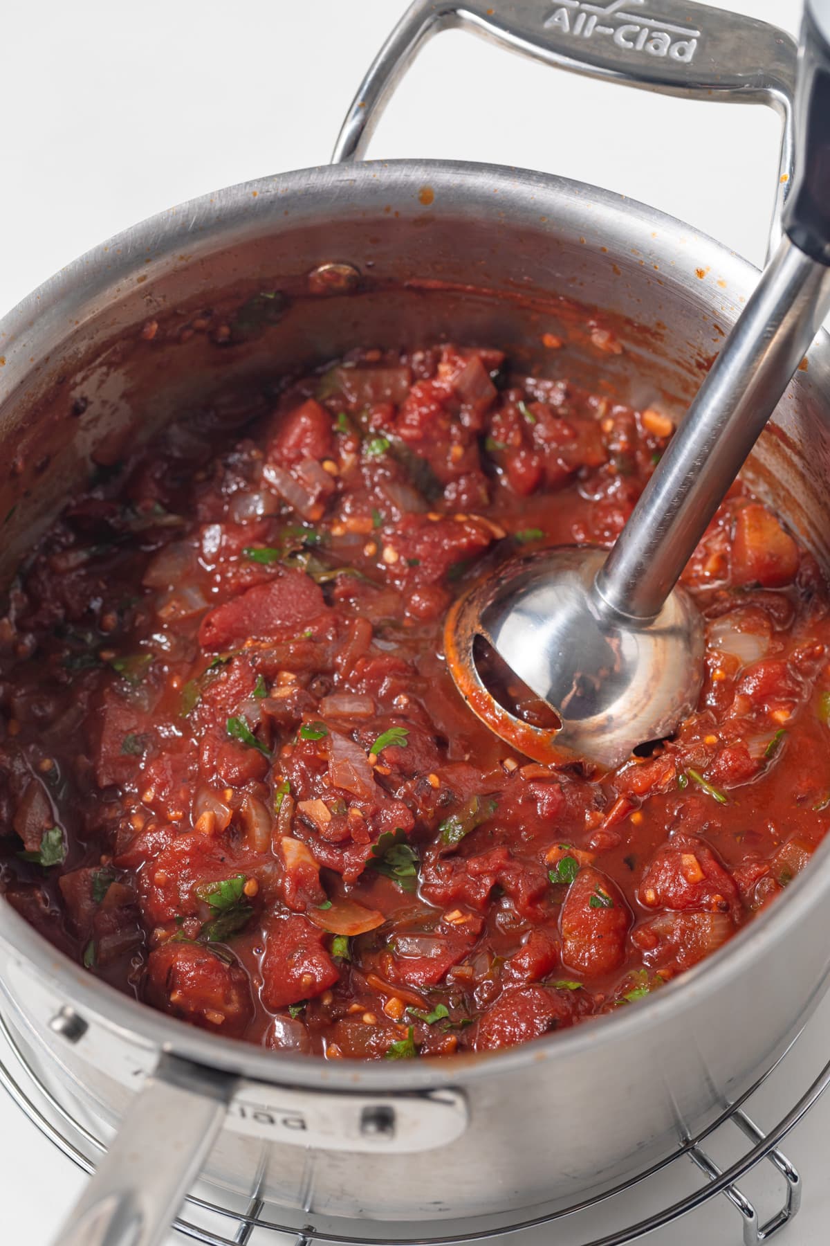 Immersion blender in pan of pasta sauce.