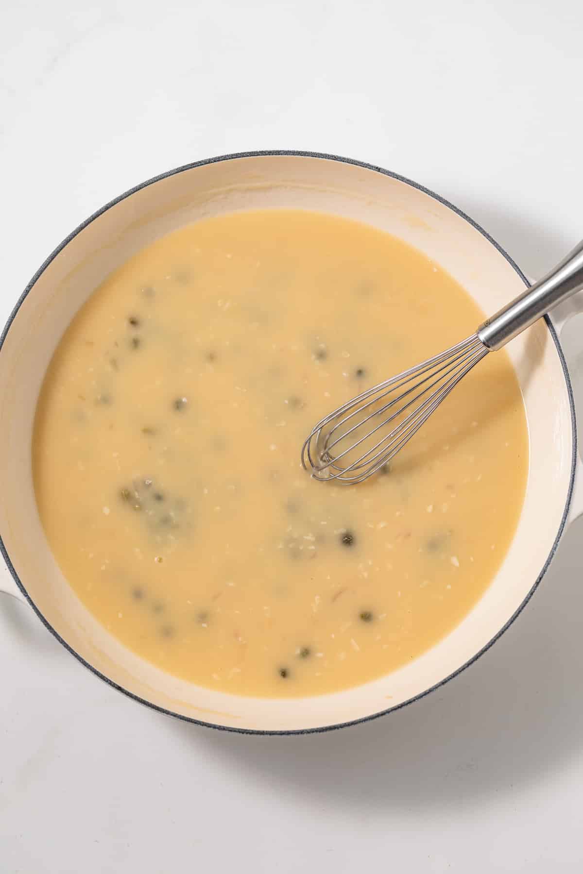 Piccata sauce with whisk in white pan.