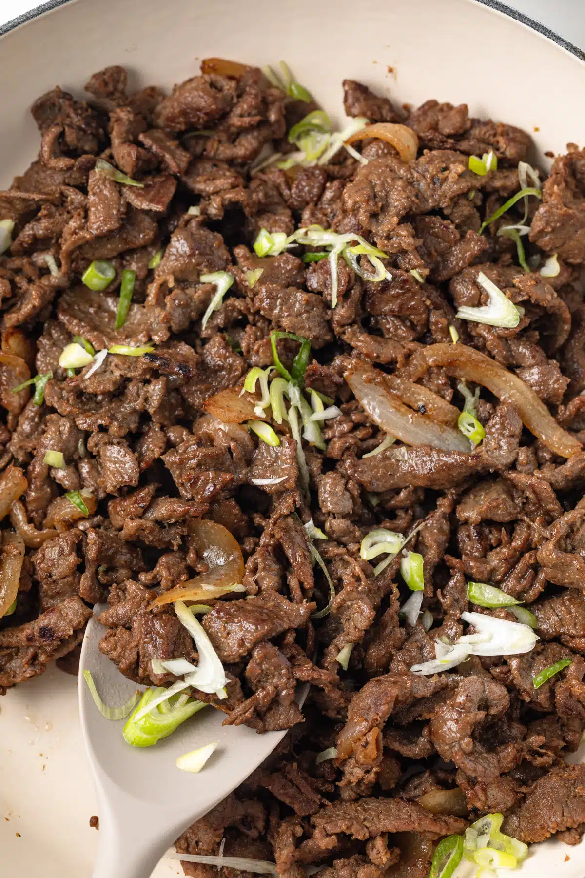 Bulgogi in topped with green onion in pan.