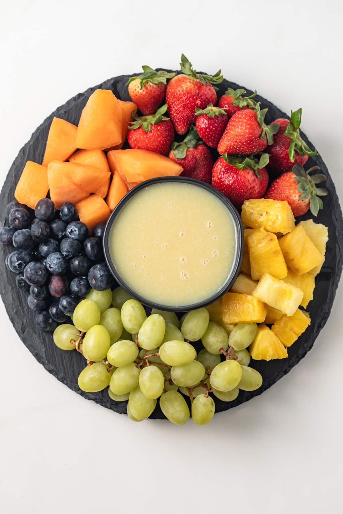 Fruit platter with white chocolate sauce in the middle.