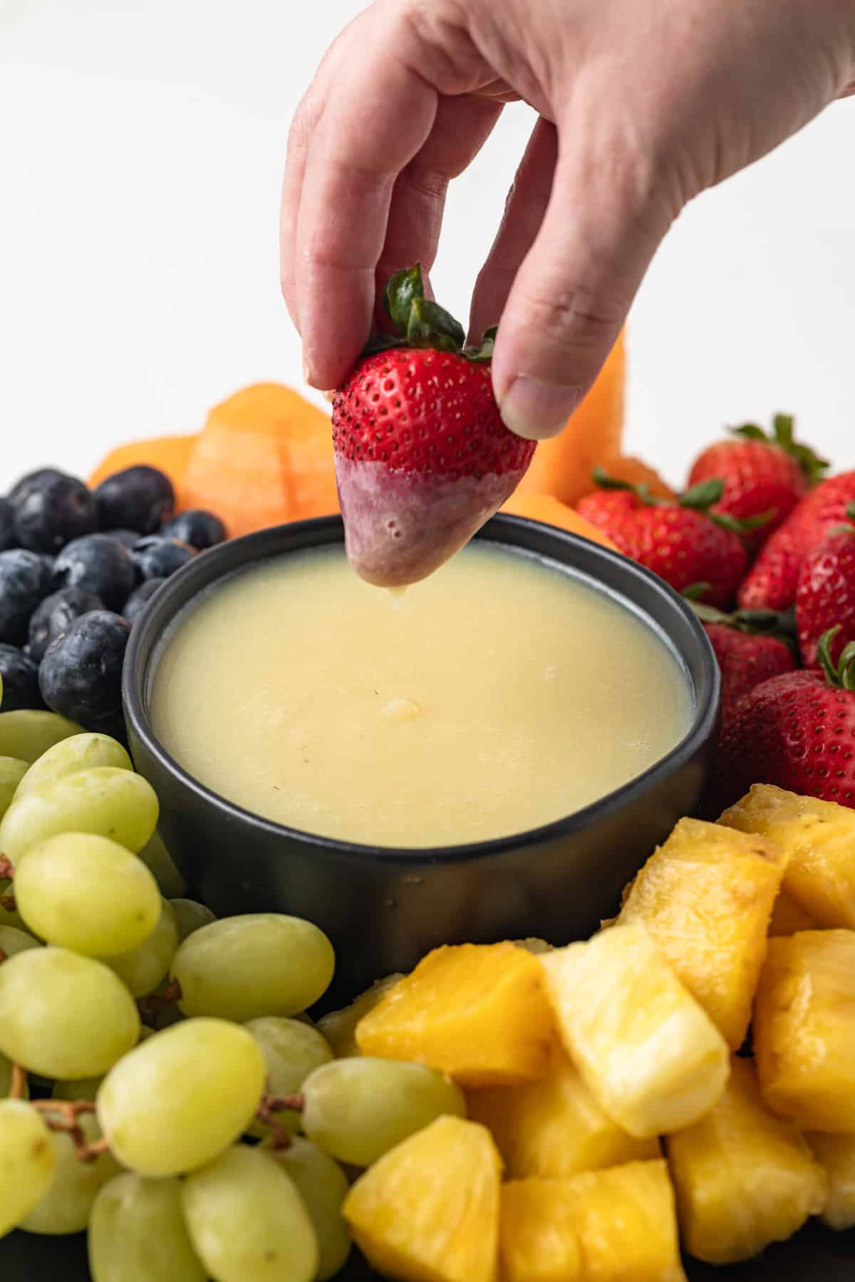 Strawberry being dipped in white chocolate sauce.