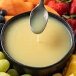 White chocolate sauce in a bowl with a spoon taking some out.