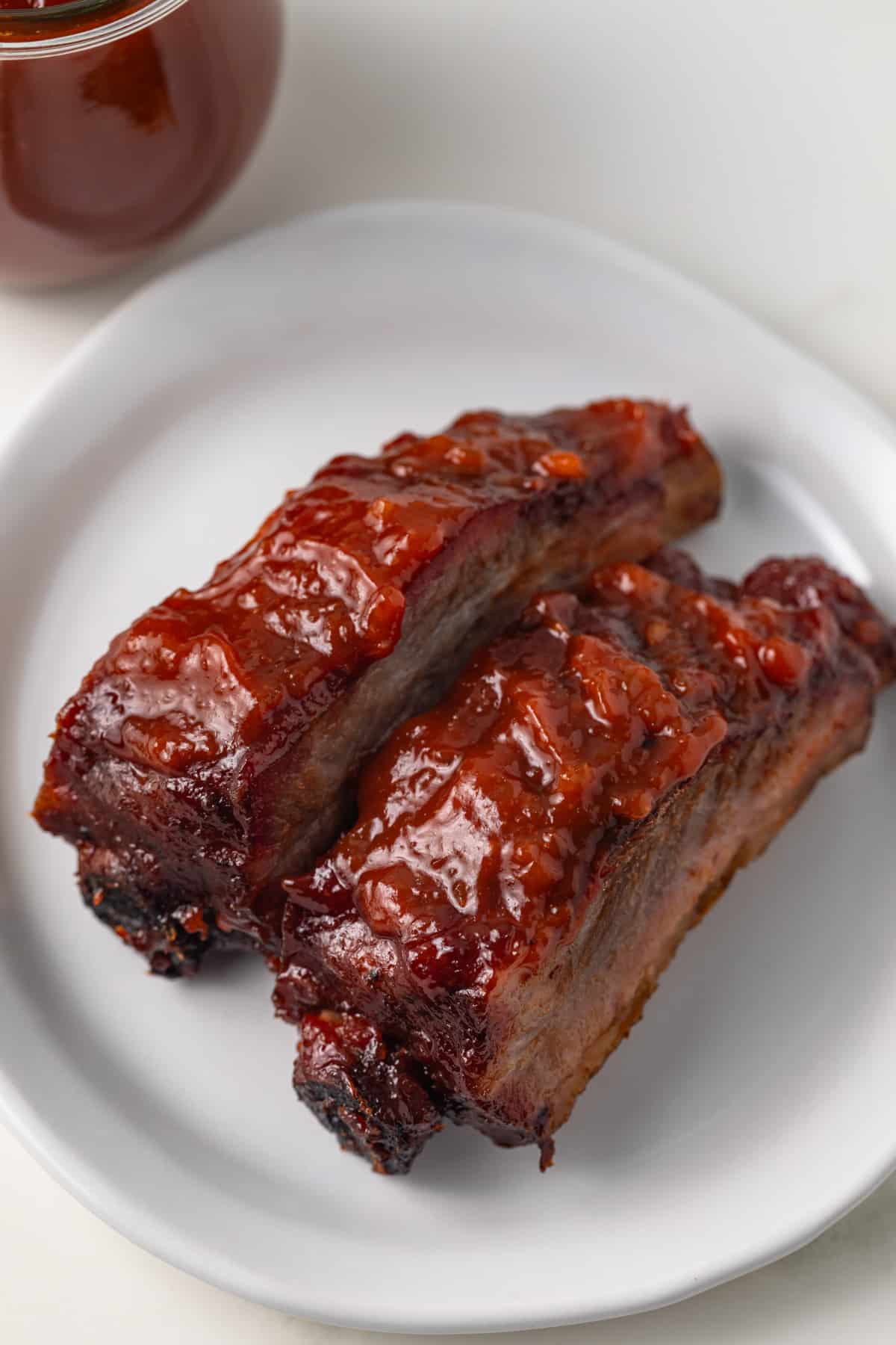 Two ribs with apple bbq sauce on white plate.