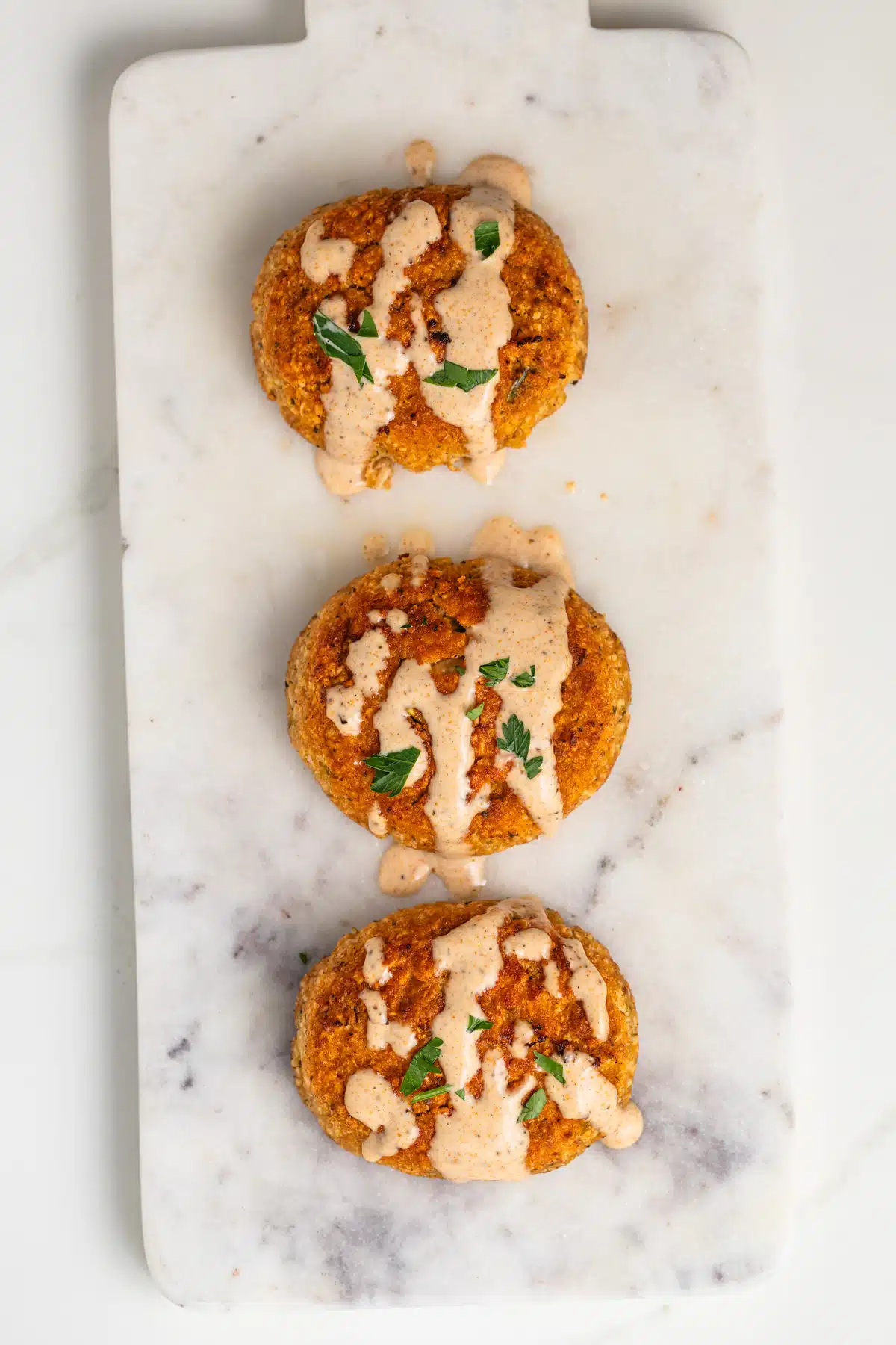 Three crab cakes drizzled with crab cake sauce.