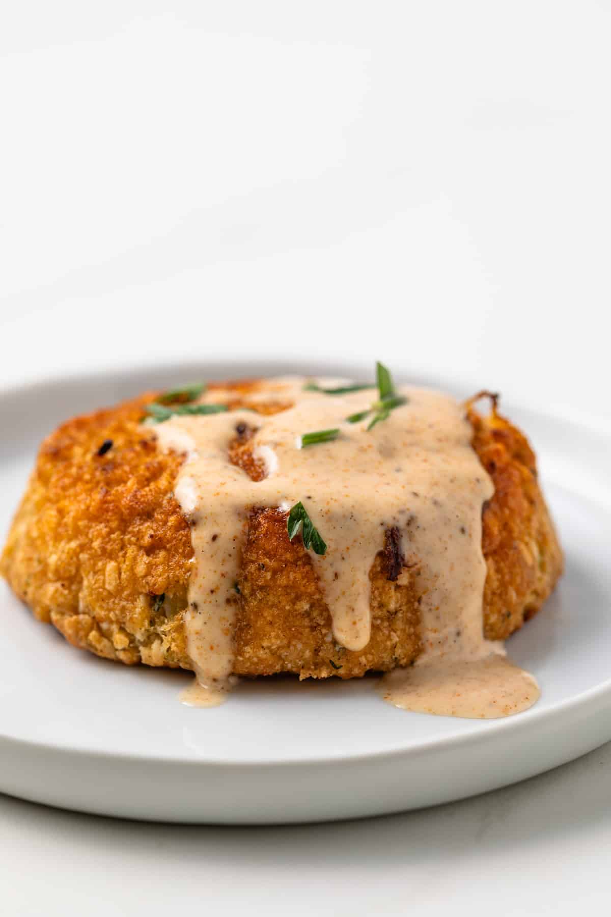 Crab cake sauce drizzled over crab cake on plate.