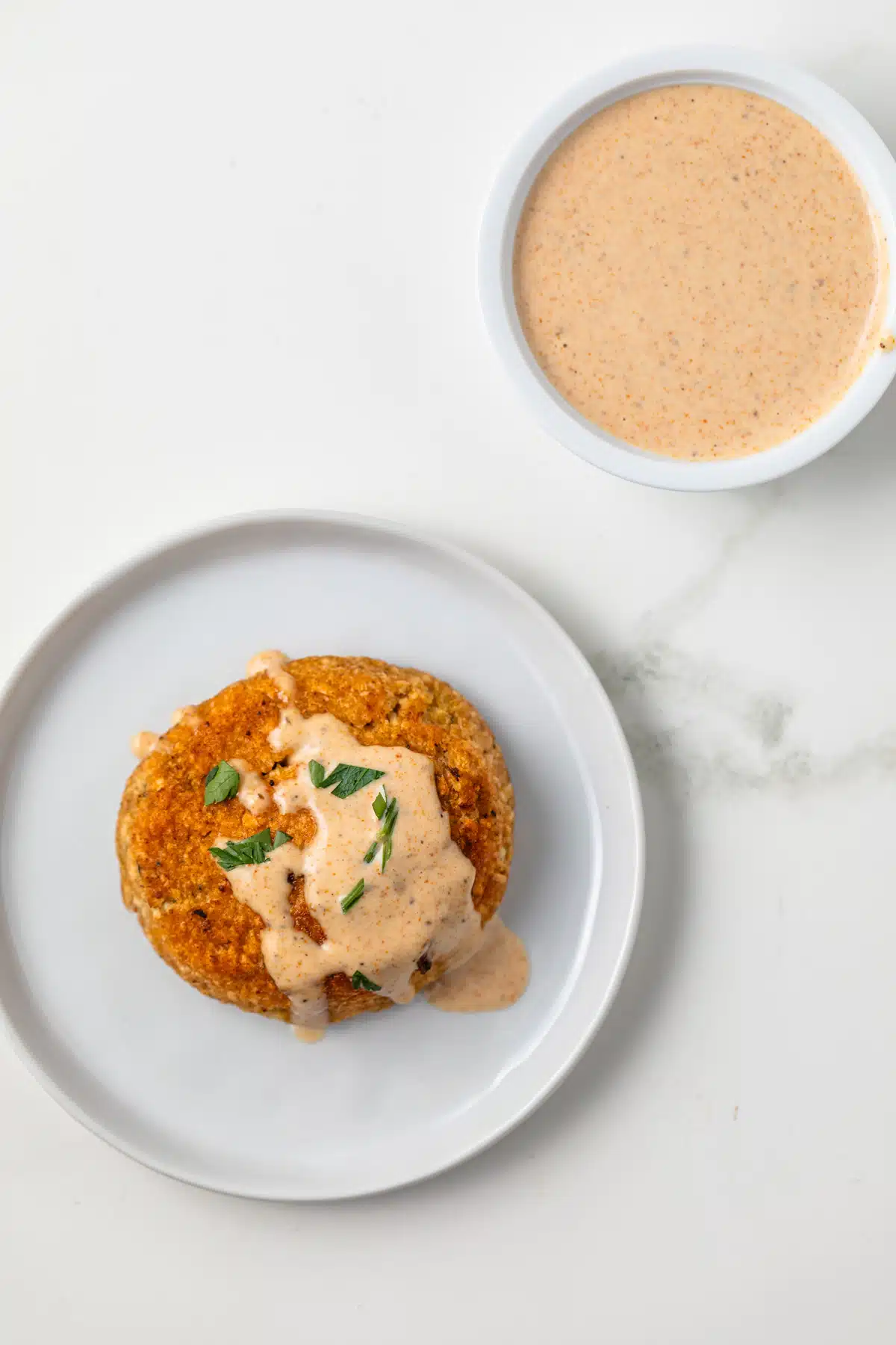 Overhead of crab cake on place with sauce in ramekin.