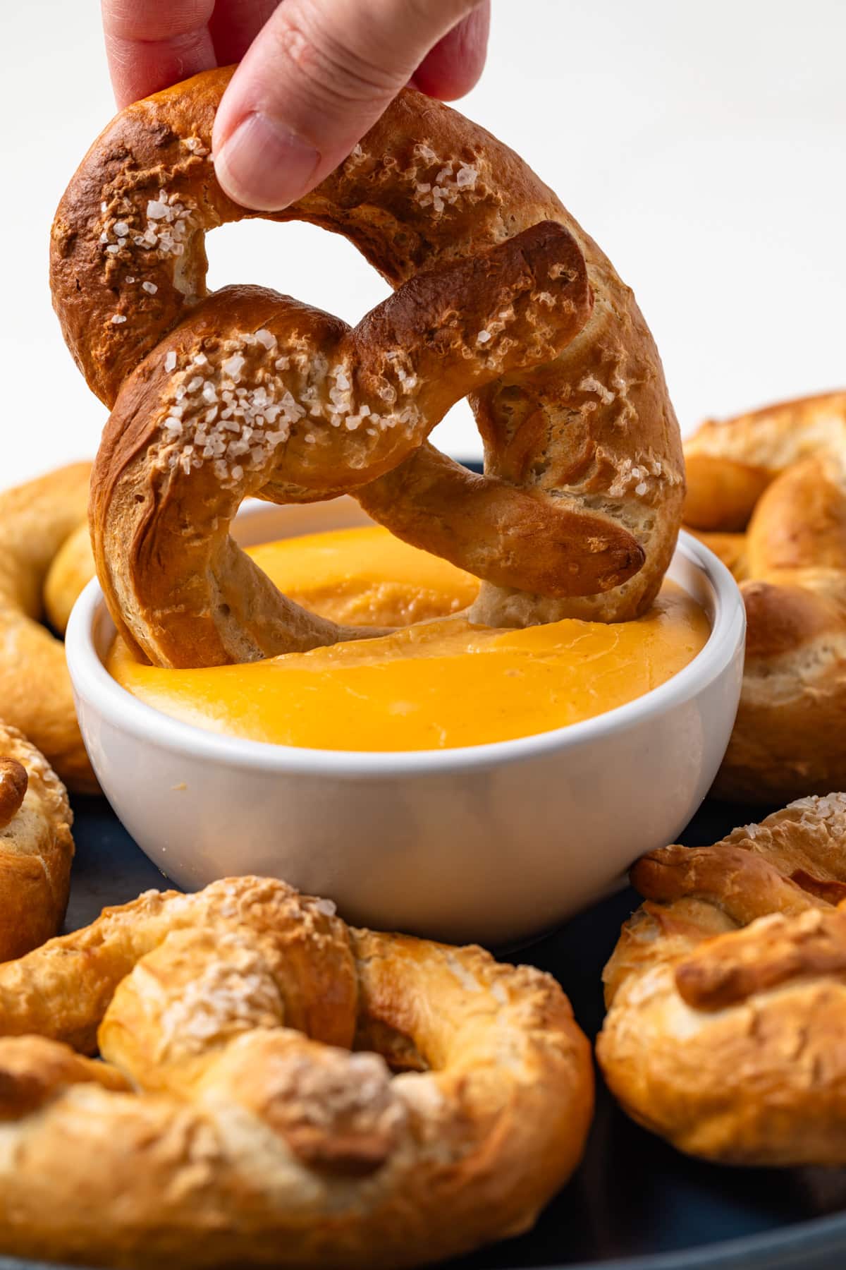 Pretzel being dipped into a small bowl of beer cheese.