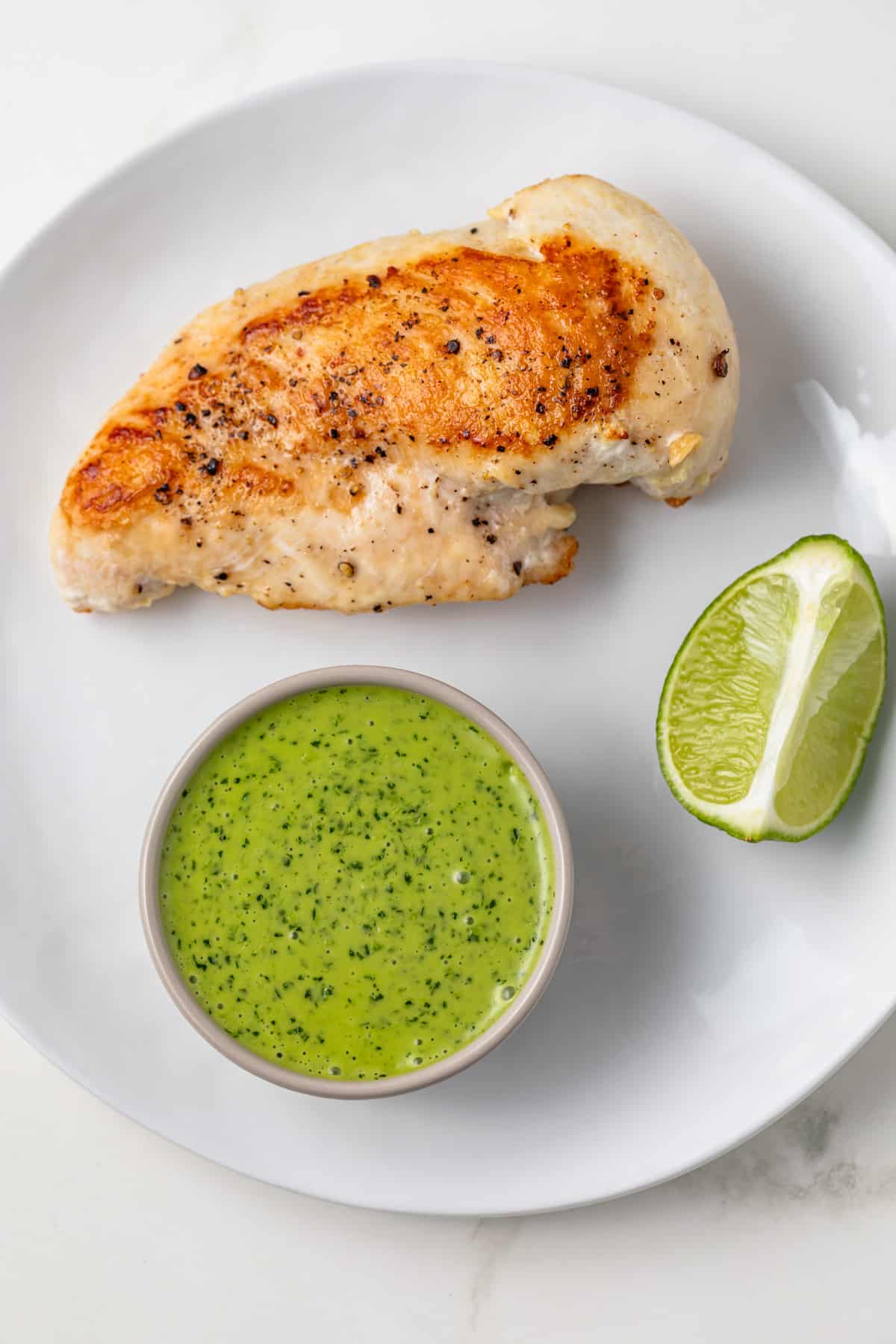 Mojo sauce in a bowl on a plate with grilled chicken.