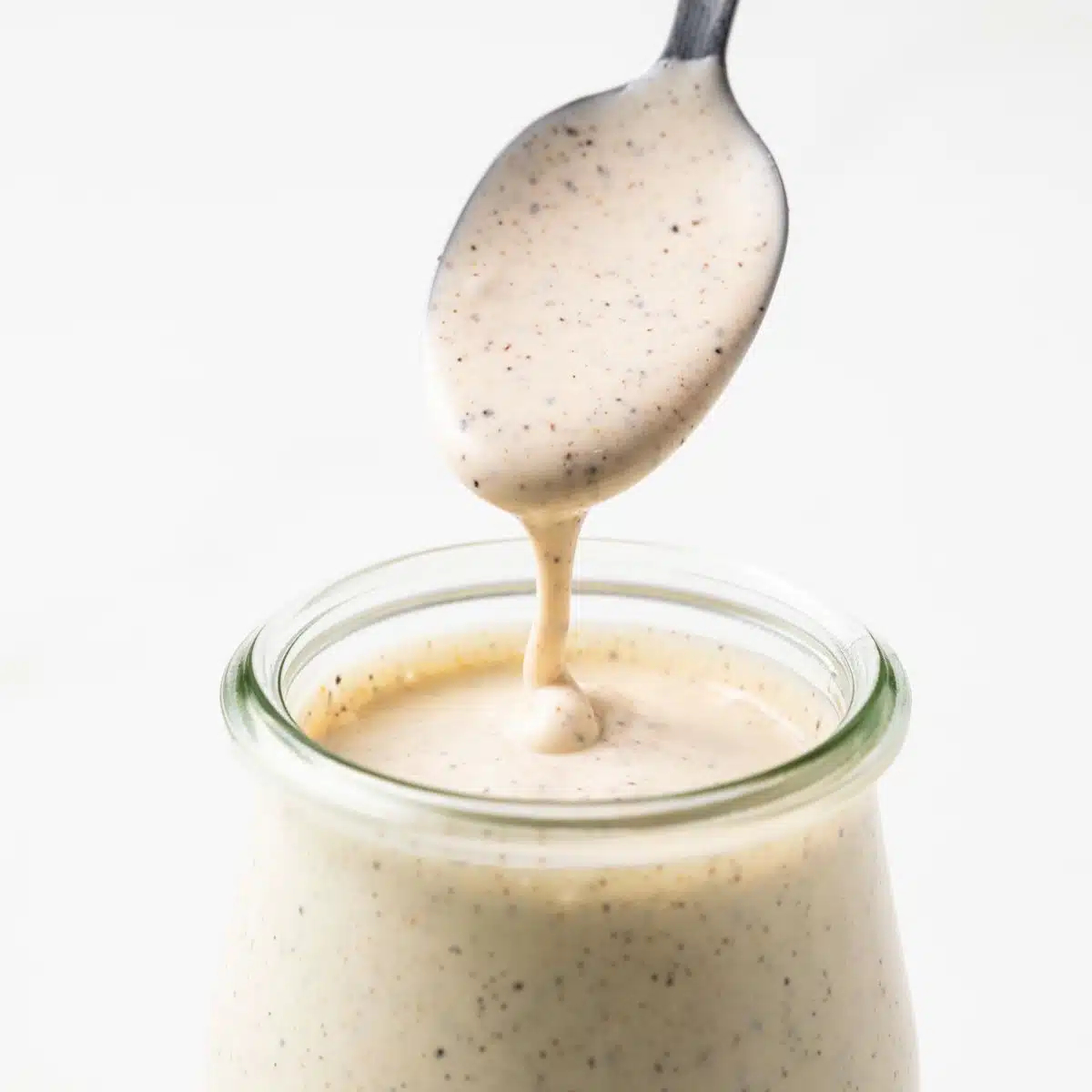 Alabama white sauce on a spoon above a jar.