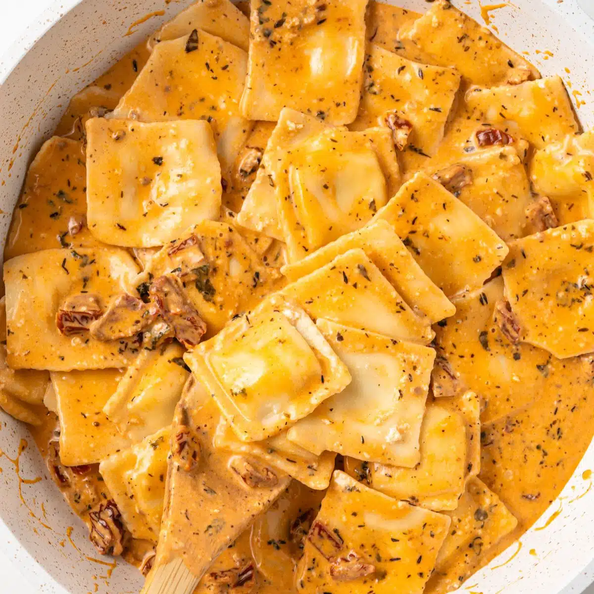 Creamy sun dried tomato sauce over ravioli in a pot.