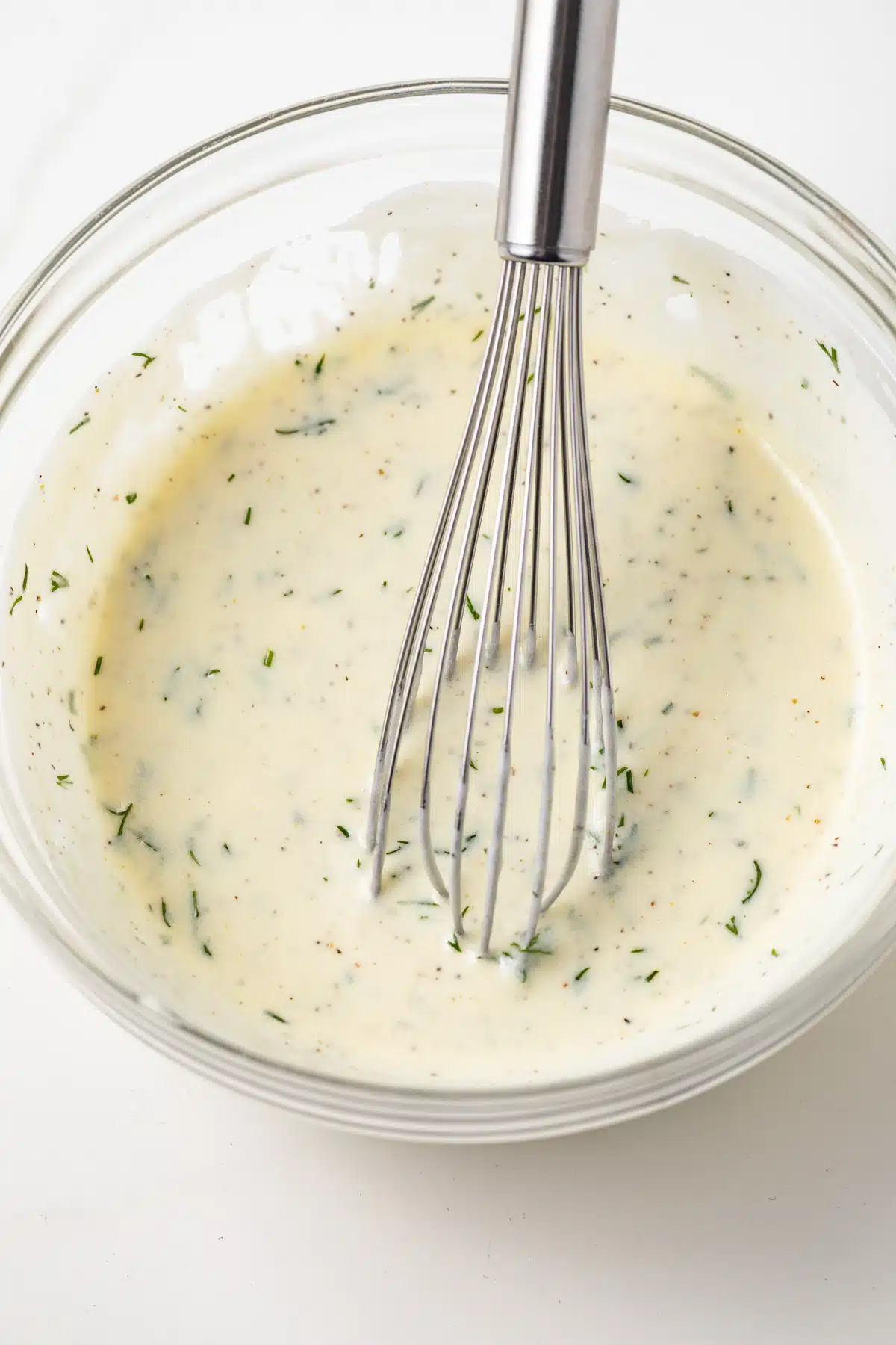 Yogurt salad dressing in a bowl with a whsisk.