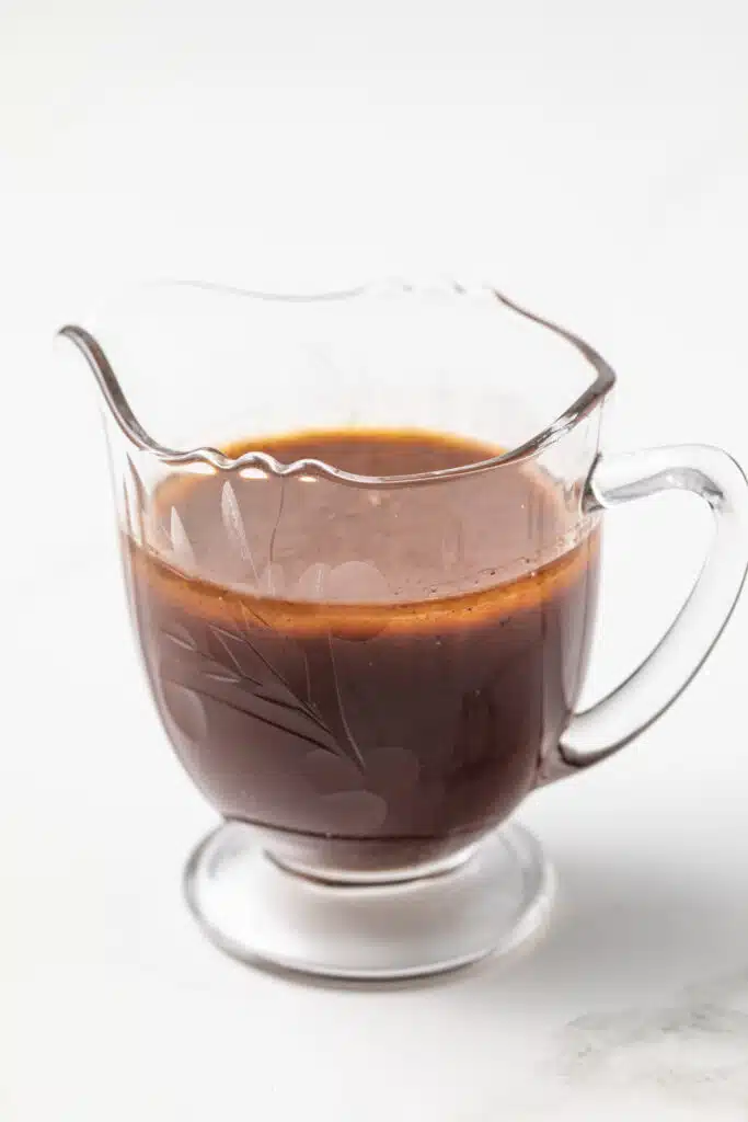 Side view of bordelaise sauce in glass gravy boat.