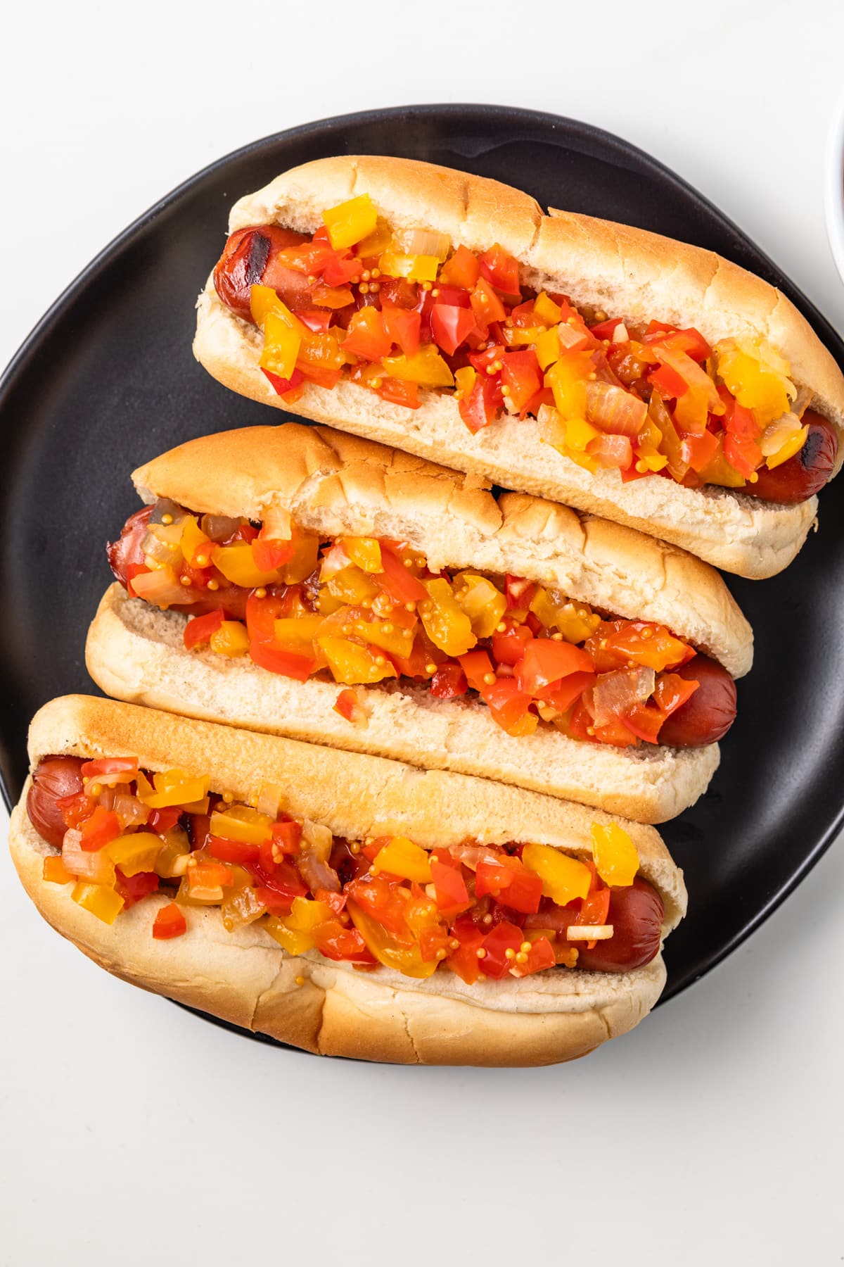 Sweet pepper relish over hot dogs on black plate.