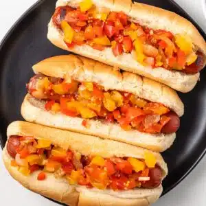 Sweet pepper relish over hot dogs on black plate.