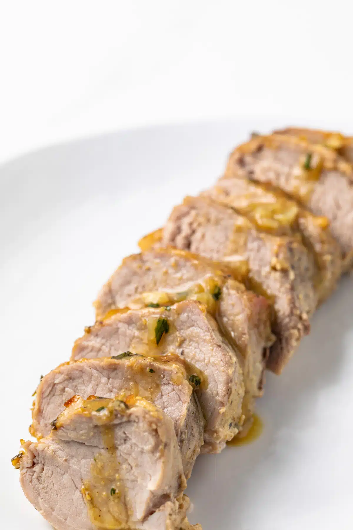 Angled view of sliced pork tenderloin drizzled with maple mustard sauce.