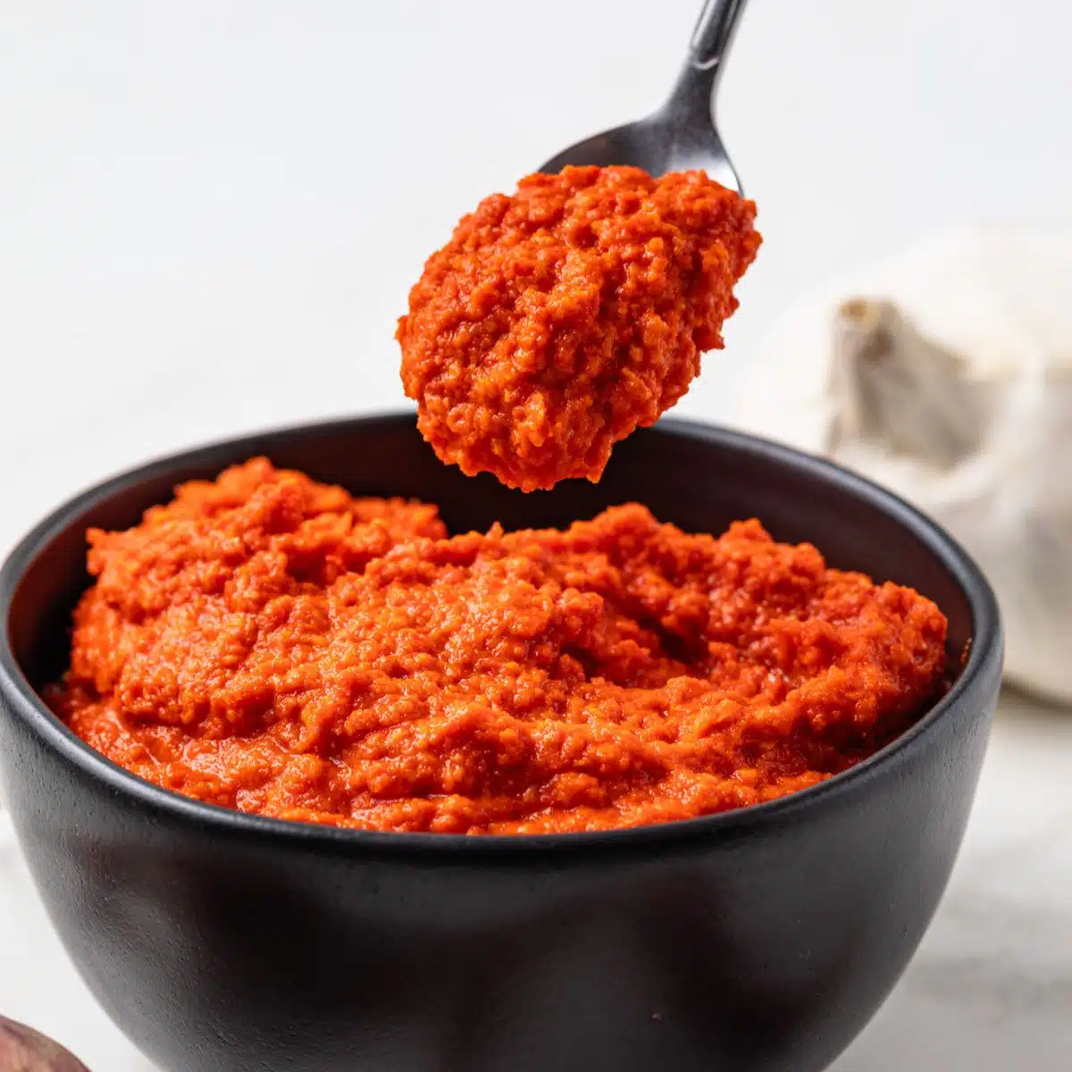 Side view of sambal oelek in a bowl with a spoon.