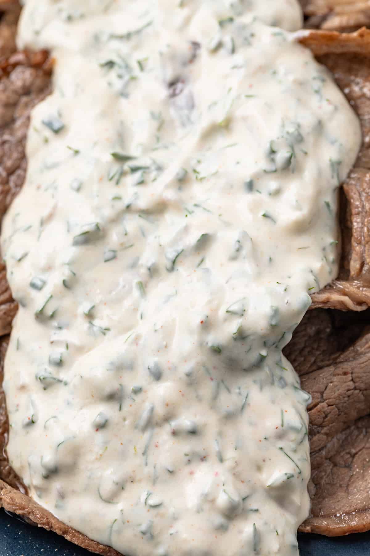 Close up of creamy herb sauce over thin sliced beef.