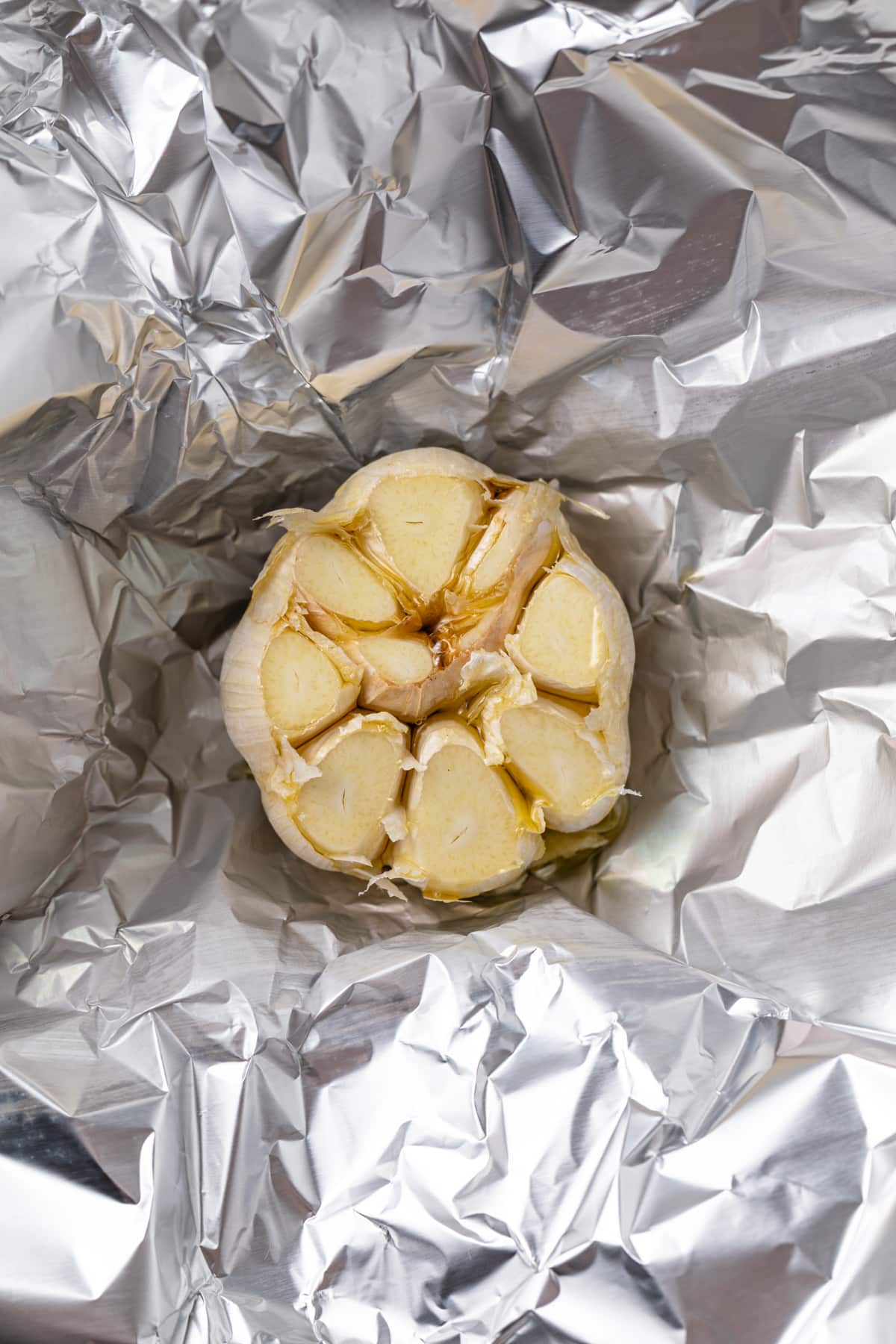 Garlic bulb with the top cut of on a piece of foil.