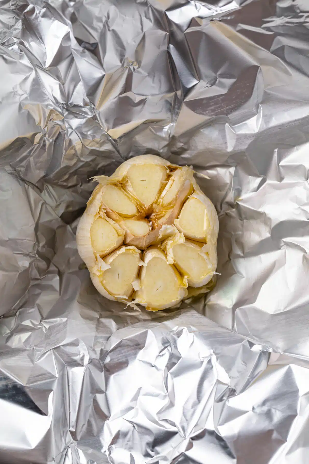 Garlic bulb with the top cut of on a piece of foil.