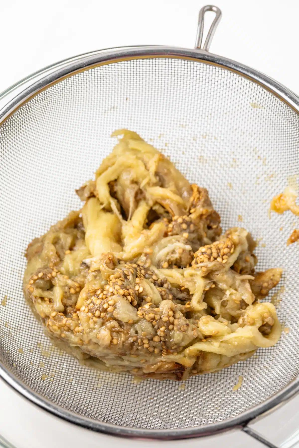 Cooked eggplant in a fine mesh seive.