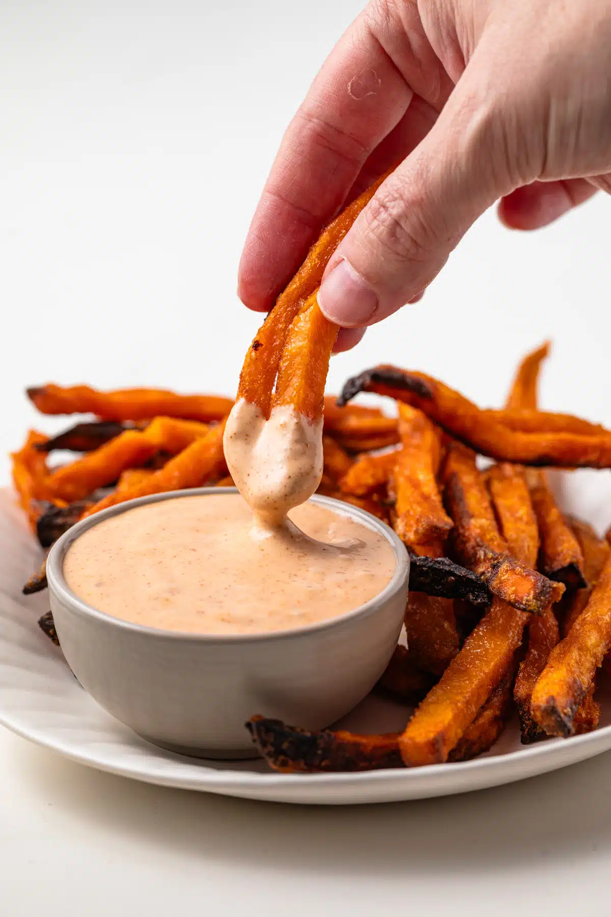 Sweet potato fries being dipped in dipping sauce.