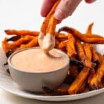 Sweet potato fries being dipped in dipping sauce.