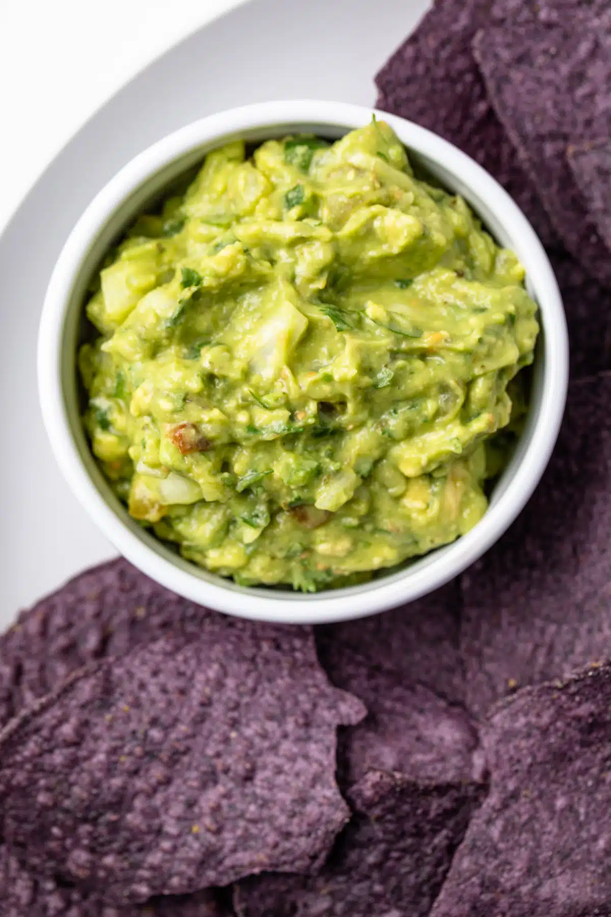 Salsa verde guacamole in a white bowl with tortilla chips.