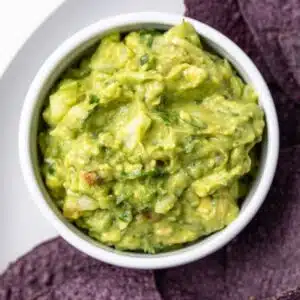 Salsa verde guacamole in a white bowl with tortilla chips.