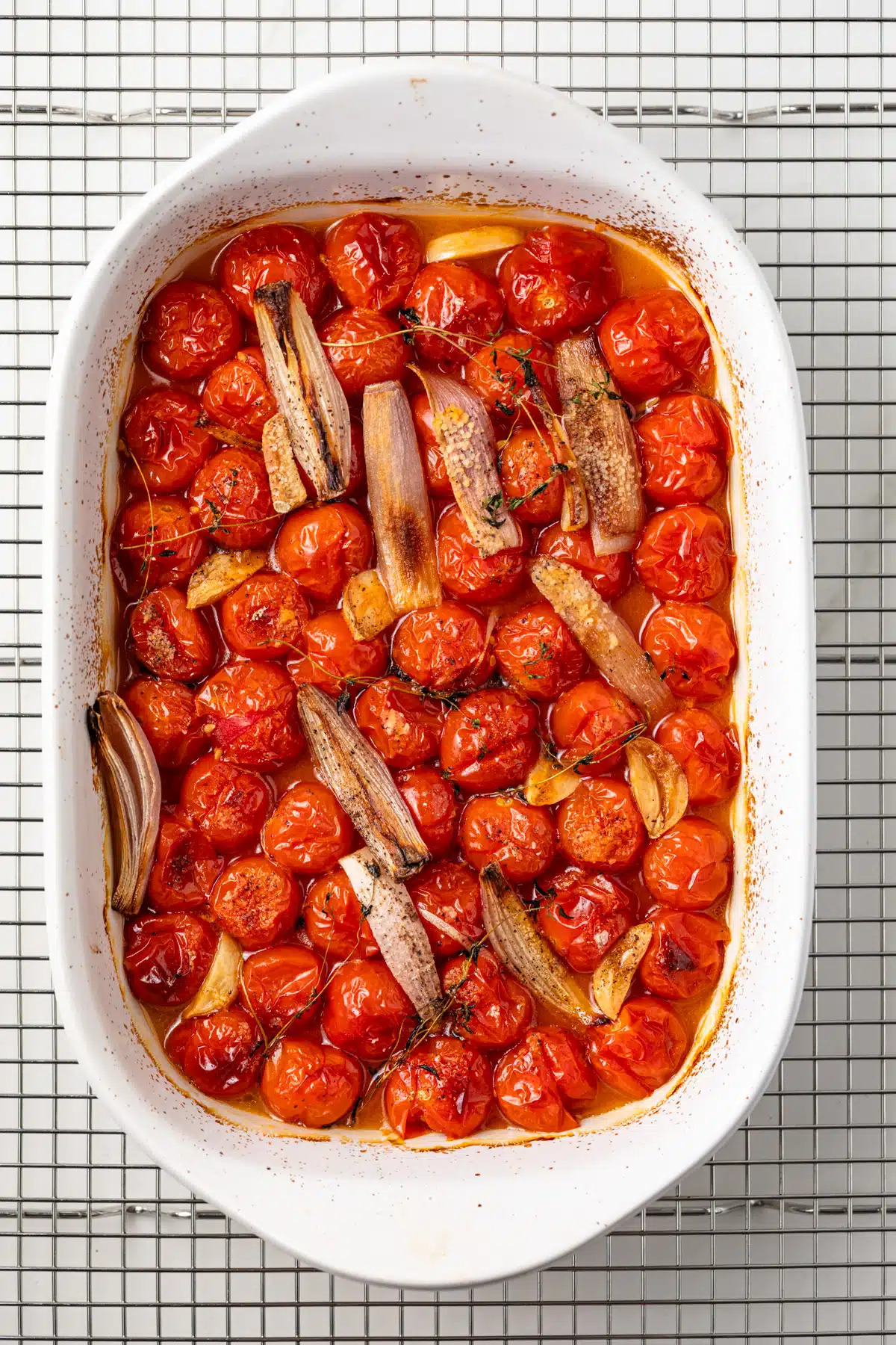 Roasted tomatoes, shallots, and garlic in a white dish.