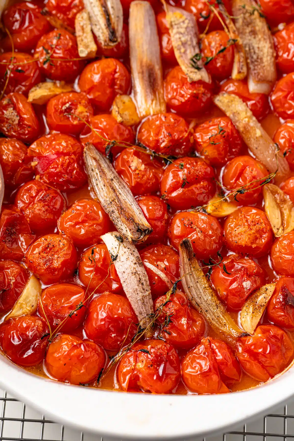Close up of roasted tomatoes, shallots, and garlic in a white dish.